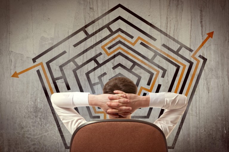 A man sitting in front of an imaginary maze on a wall, contemplating his next business steps
