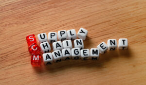 A group of dice on a table that spells 'Supply Chain Management' on 3 horizontal lines and 3 red dice for SCM vertically.